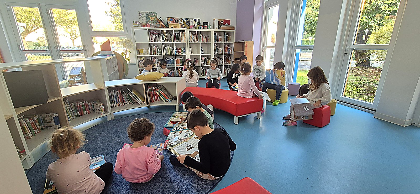 Bambini dell'Infanzia seduti in cerchio che leggono in biblioteca